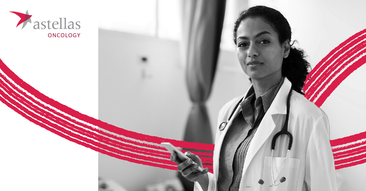 female doctor in white coat stands holding a cellphone, Astellas Oncology logo in background